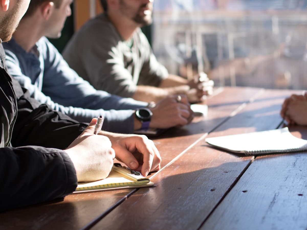 A small team around a table in a working meeting, taking notes and talking.