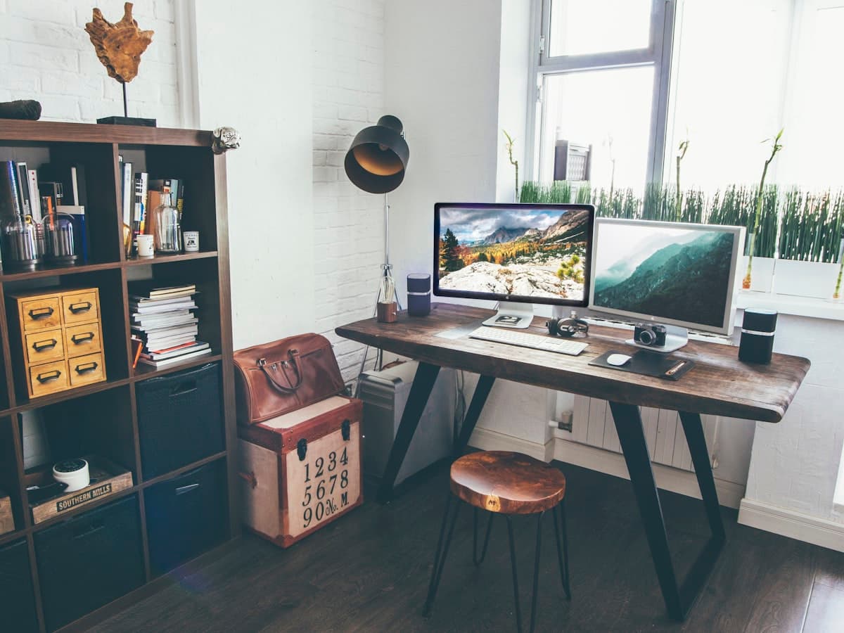 A home office desk with a monitor, shelves and a lamp, set up for daily work.
